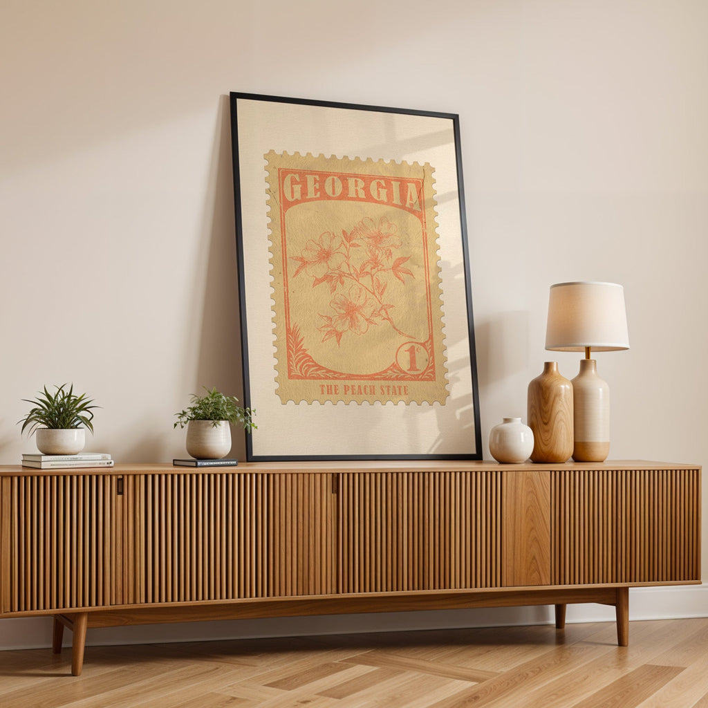 Georgia state flower print in a black frame leaning on a fluted wood credenza with vases and a lamp