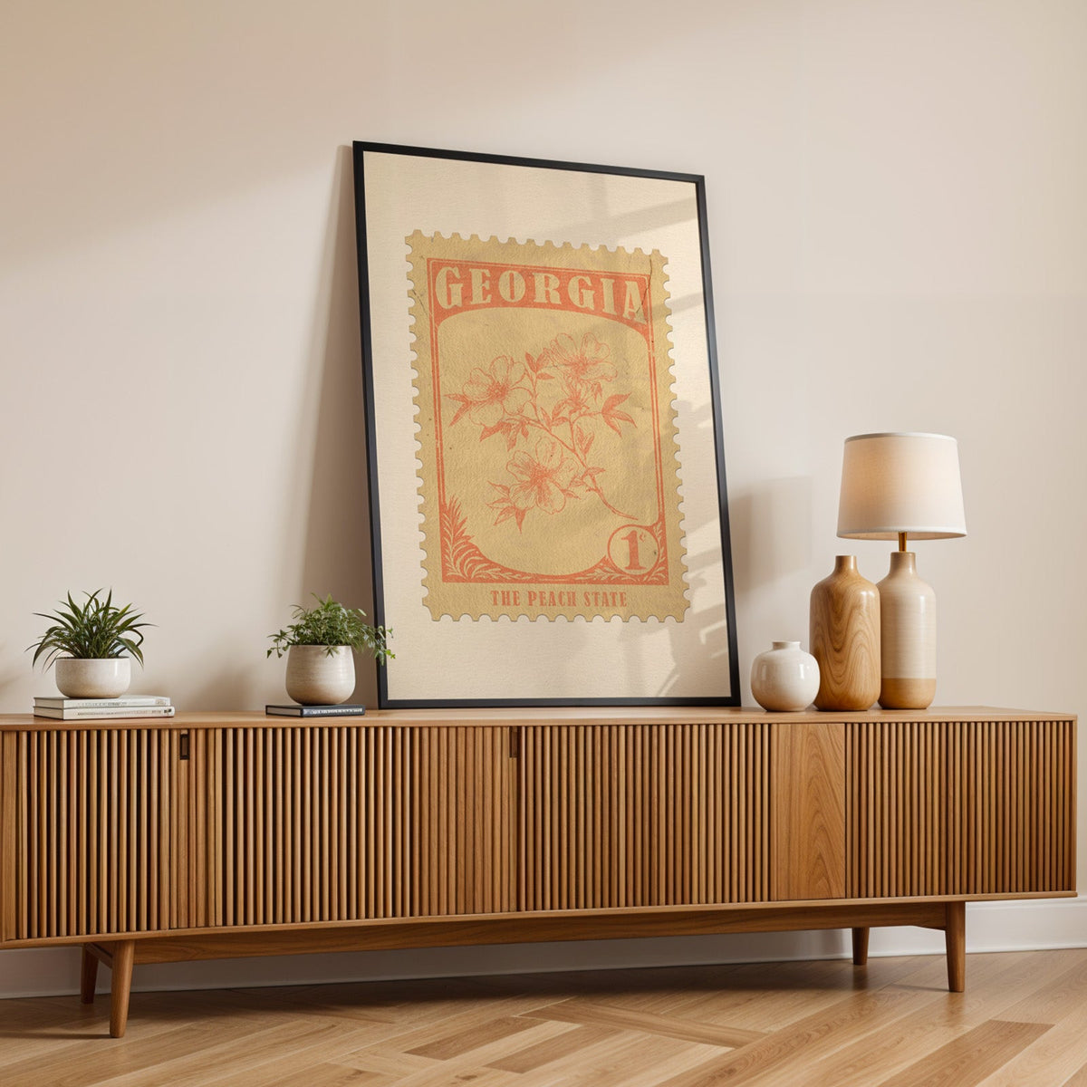 Georgia state flower print in a black frame leaning on a fluted wood credenza with vases and a lamp