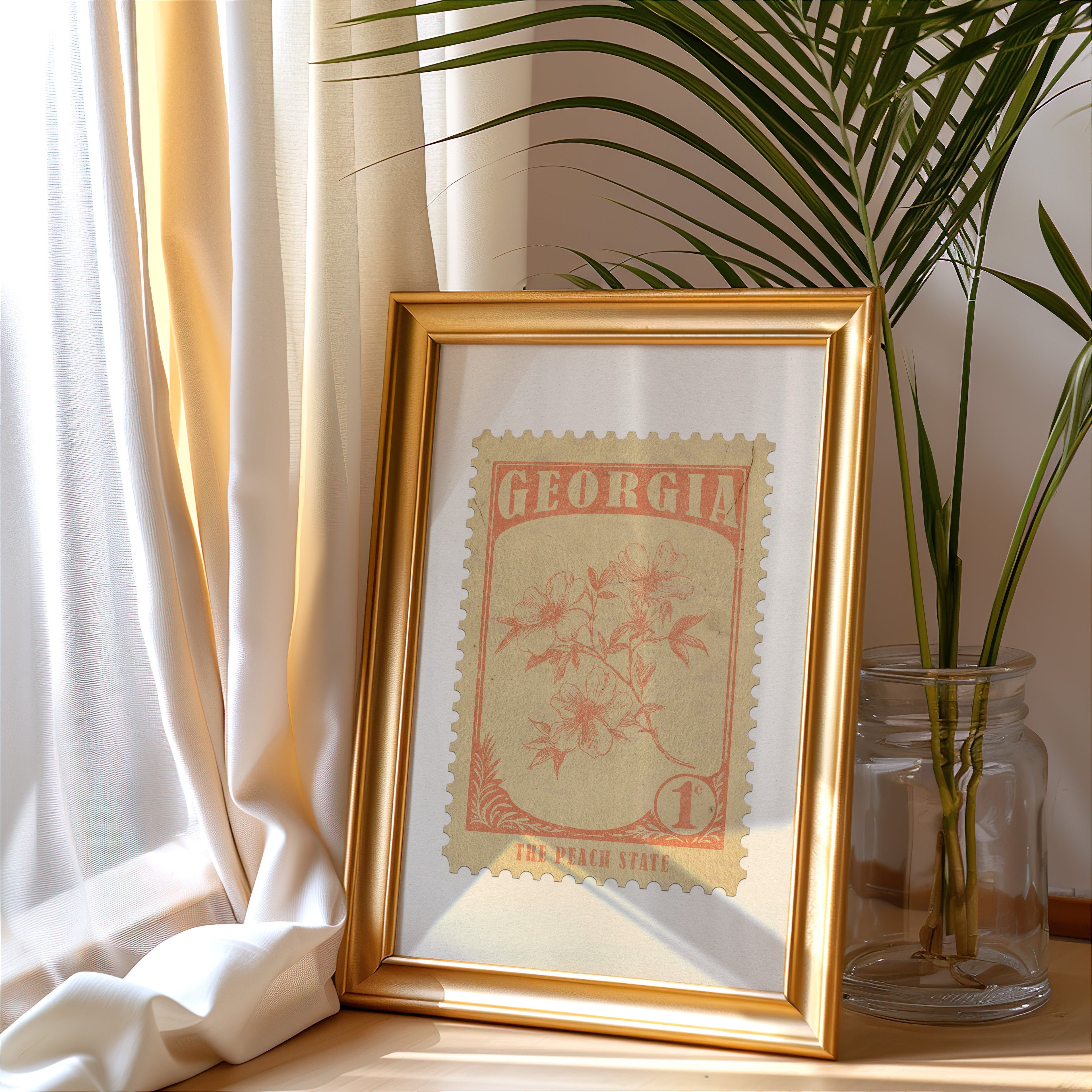 Georgia stamp print in a gold frame leaning by a cream curtain with a palm in a glass jar