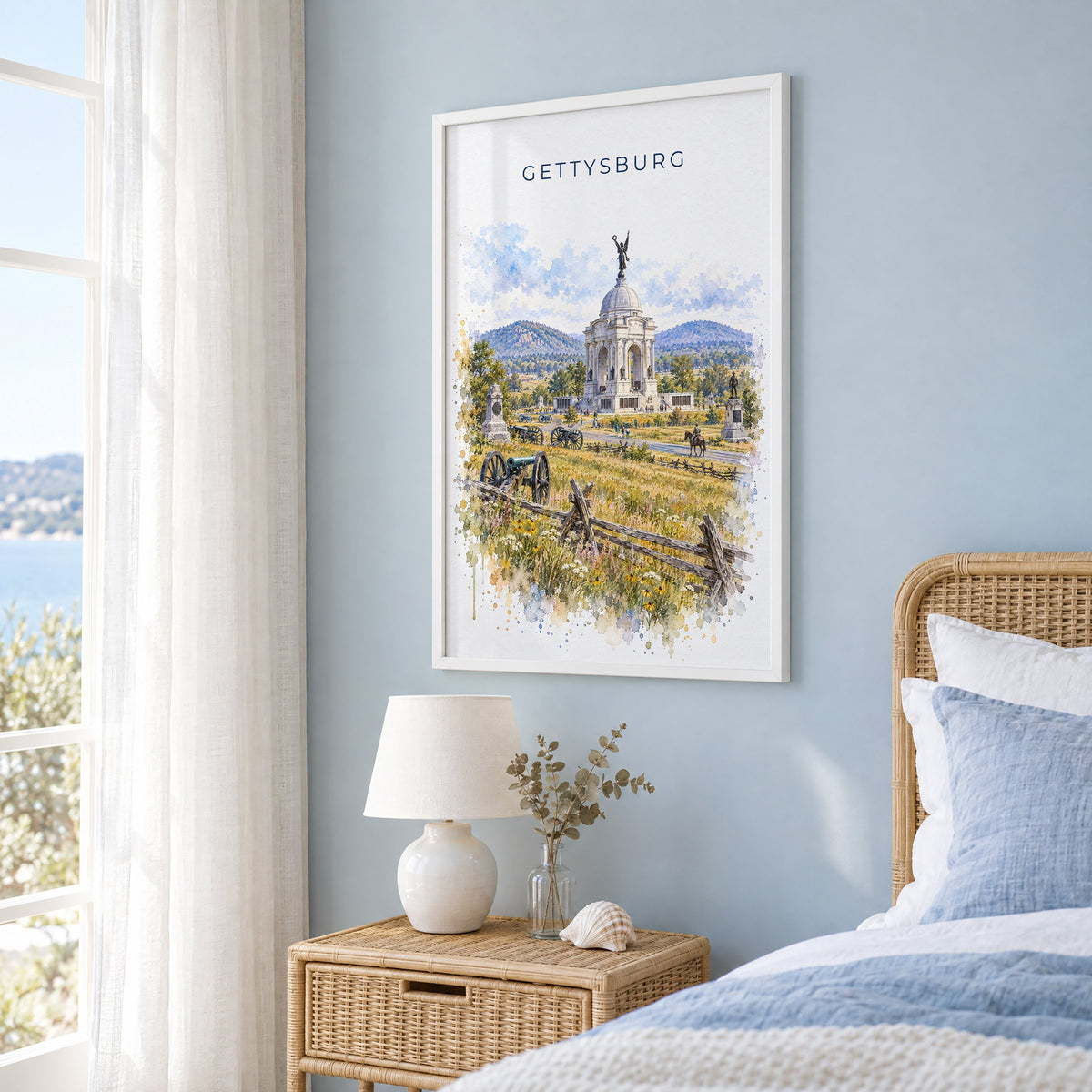 Gettysburg watercolor print in a white frame on a pale blue wall beside a rattan bed in a coastal bedroom
