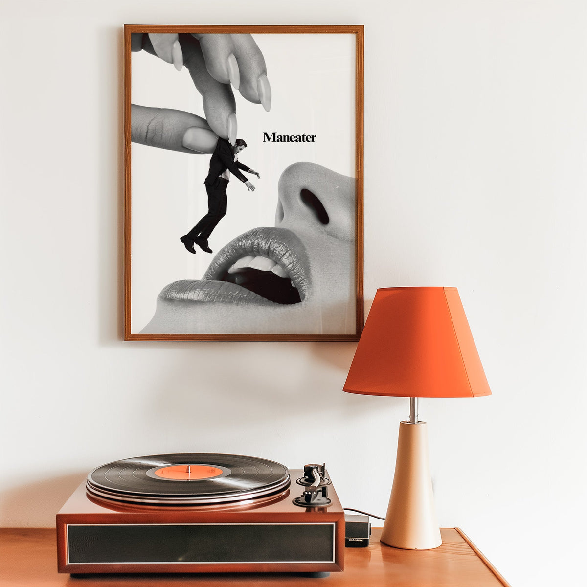 Giant hand lifting tiny suited man collage print in a walnut frame above a record player and orange lamp