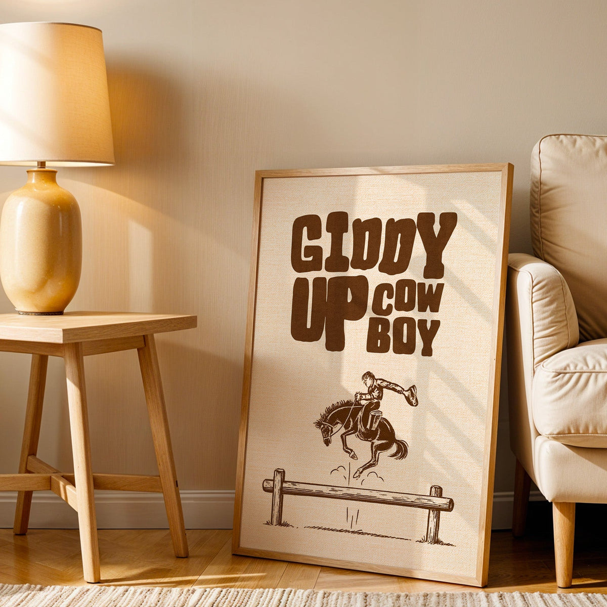 Giddy Up Cowboy cream print in an oak frame beside an amber ceramic lamp