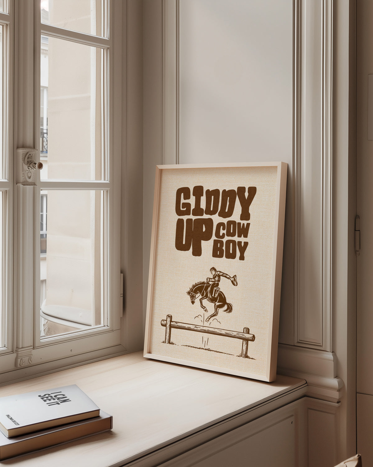 Giddy Up Cowboy cream print in a pale wood frame on a sunlit window ledge
