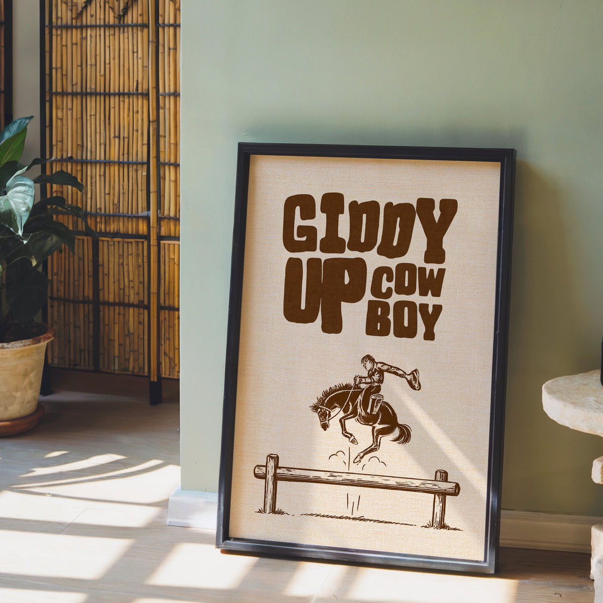 Giddy Up Cowboy cream print in a black frame leaning against a sage green wall
