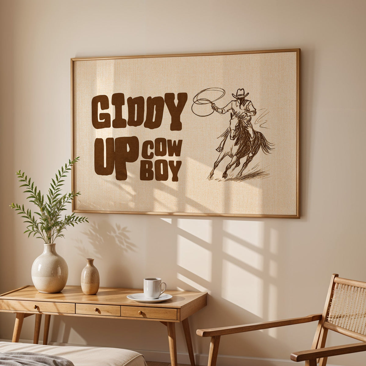 Giddy up cowboy lasso print in an oak frame above a sunlit desk with a cane chair