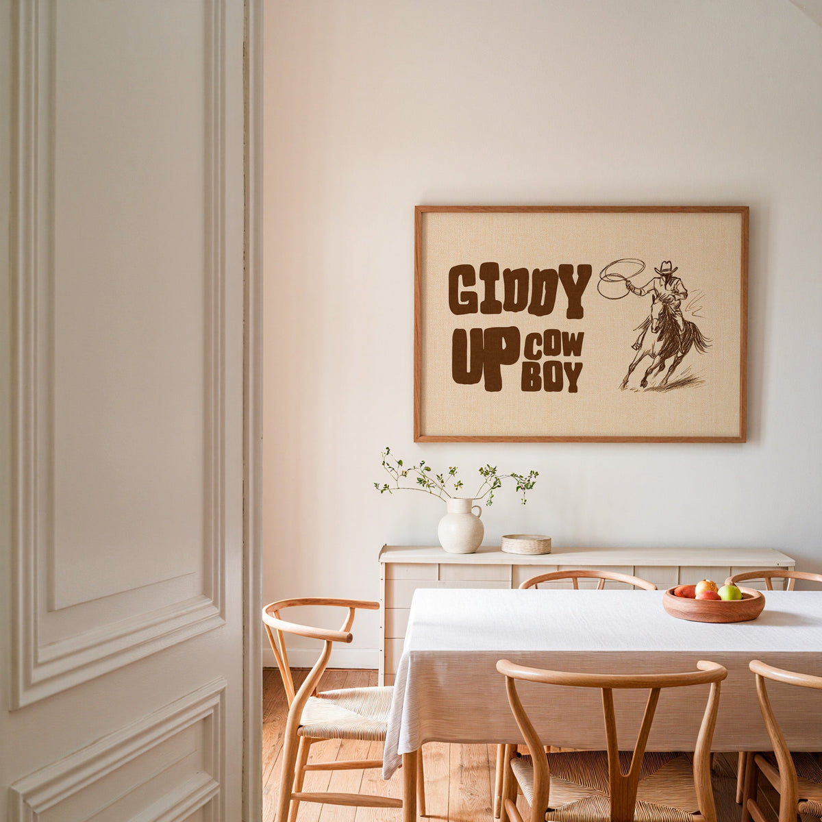 Giddy up cowboy lasso print in an oak frame above a dining table with wishbone chairs