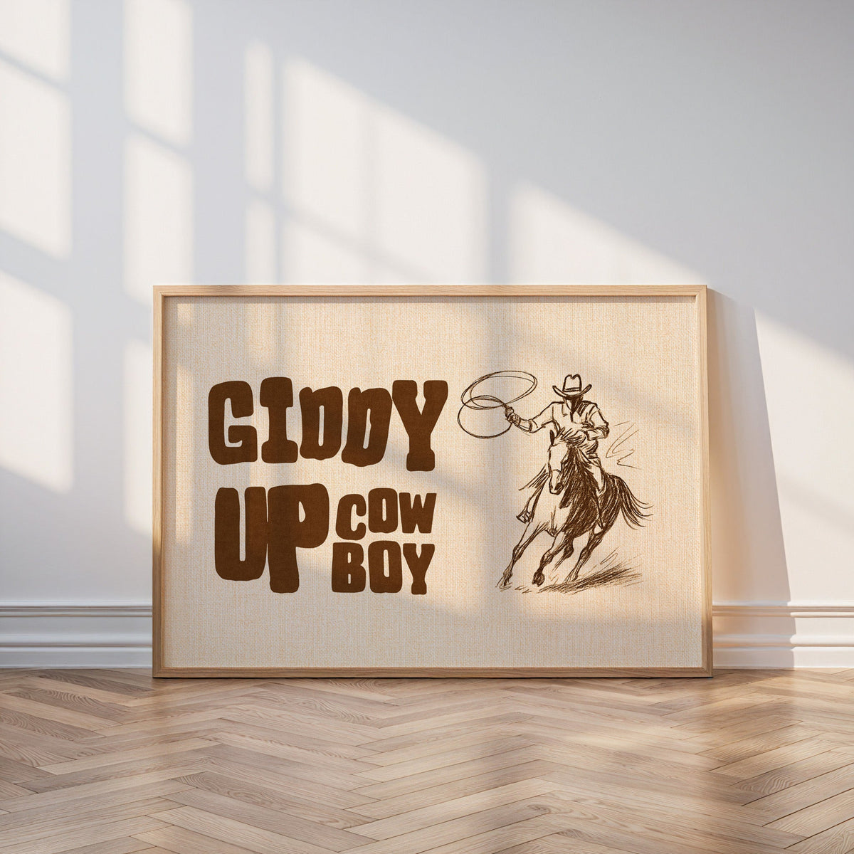 Giddy up cowboy lasso print in an oak frame on a parquet floor in window light