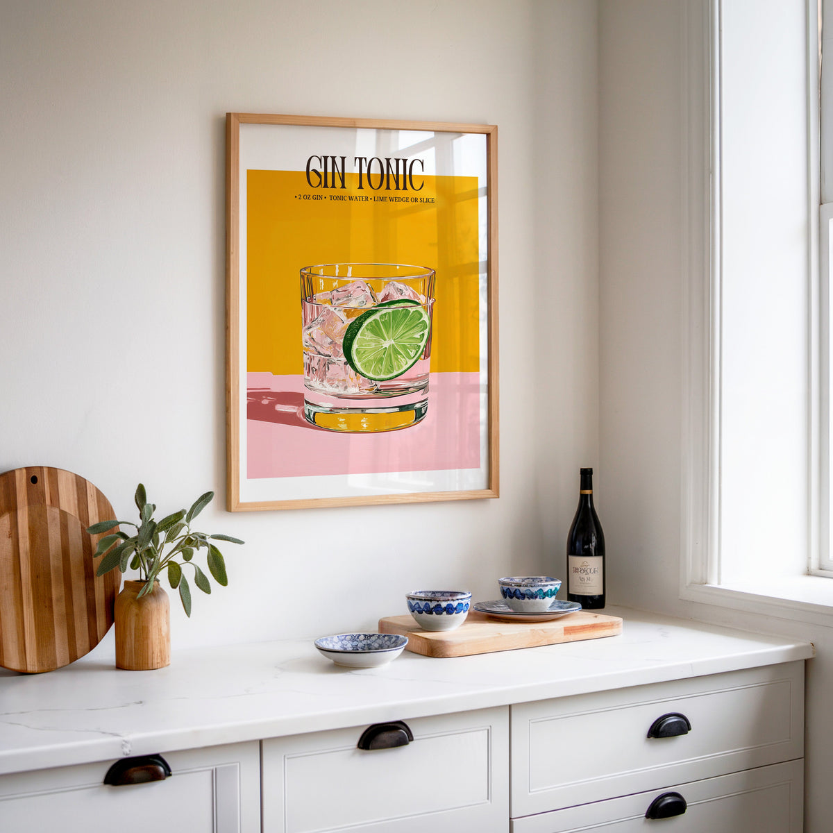 Gin and tonic recipe print in an oak frame above a white sideboard with a bottle of wine