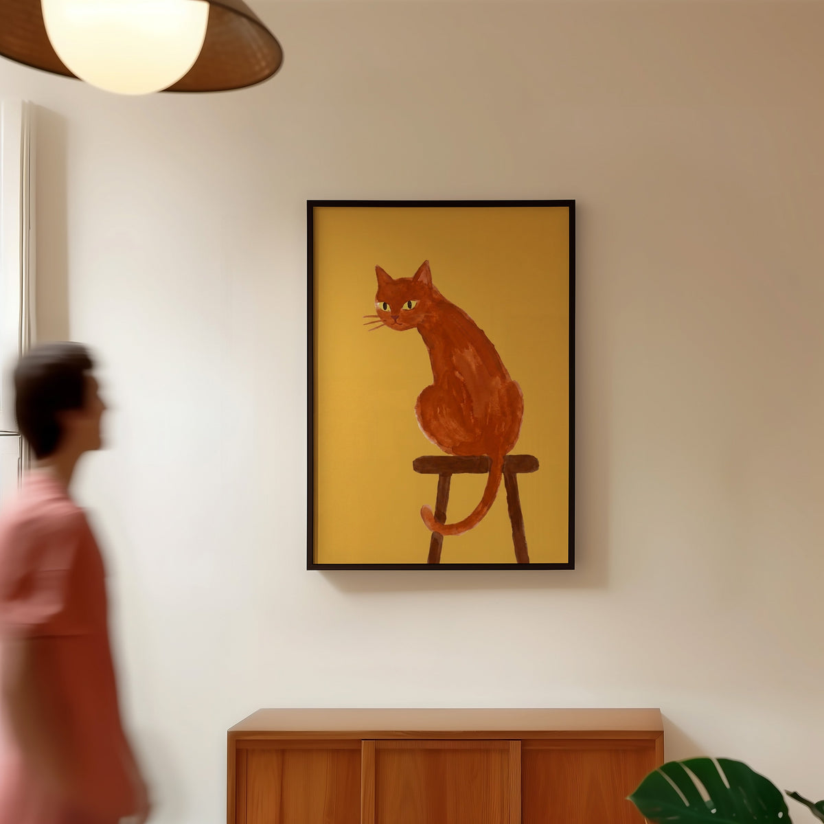 Mustard ginger cat print in a black frame in a hallway under a rattan pendant