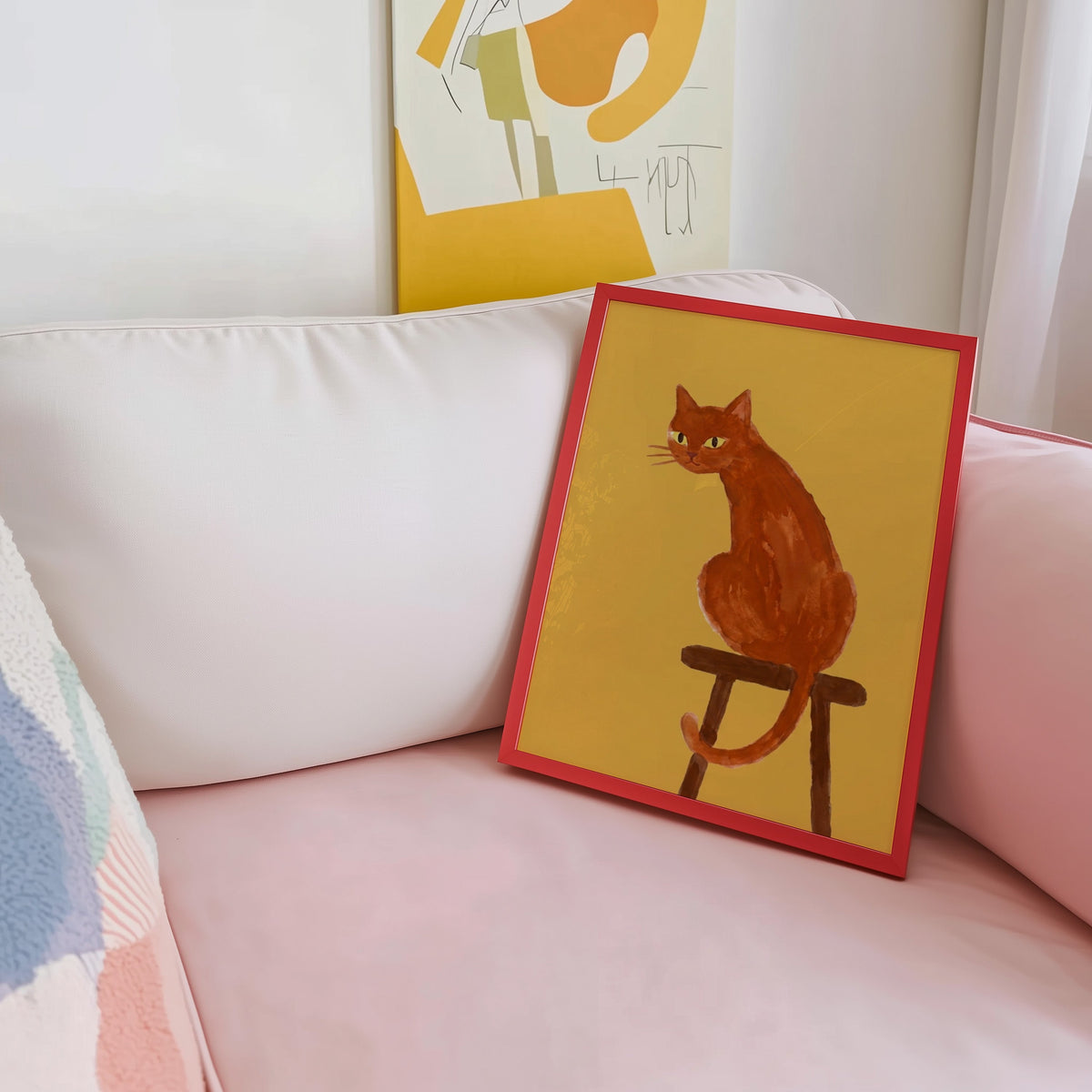 Watercolor cat portrait print shown in a red frame leaning on a blush pink sofa