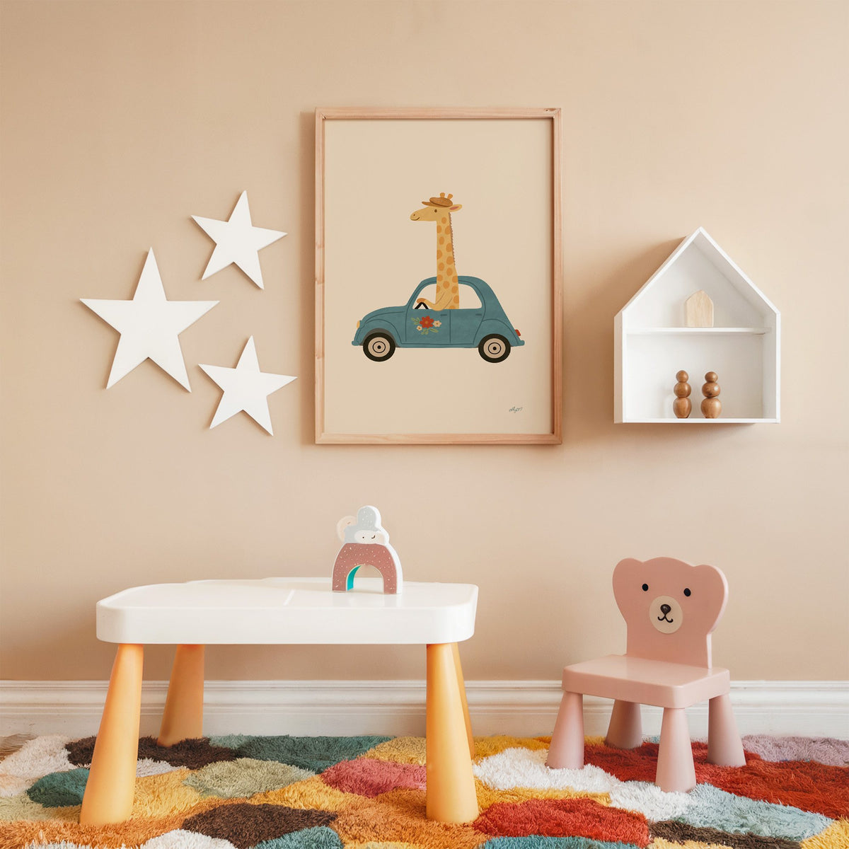 Giraffe driving a teal car nursery print in an oak frame on a peach wall above a kids table with wall stars