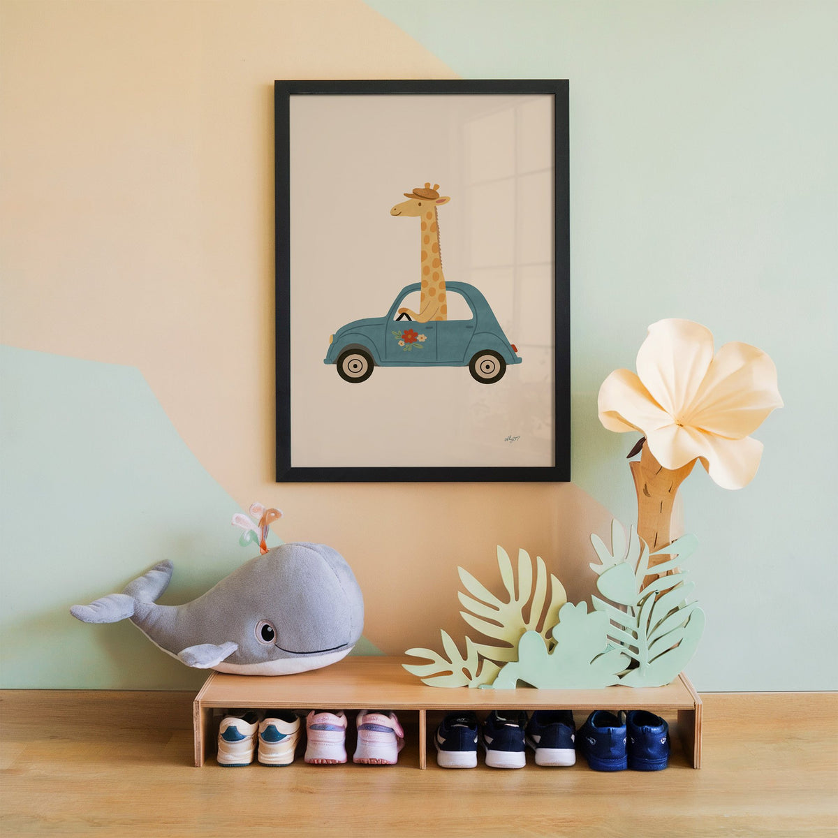 Giraffe driving a teal car nursery print in a black frame on a mint and peach wall above a whale plush
