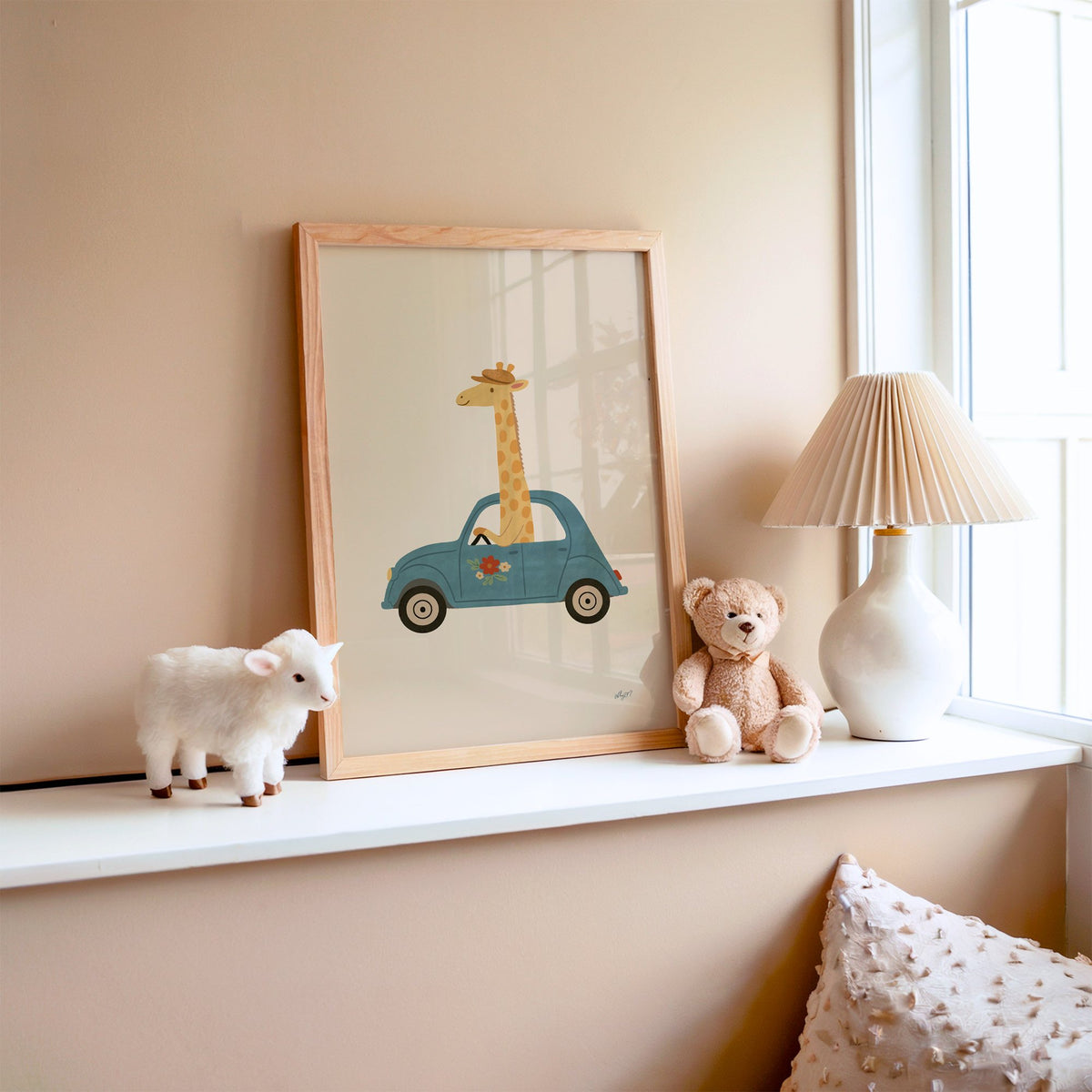 Giraffe driving a teal car nursery print in an oak frame on a window ledge with a toy lamb and teddy