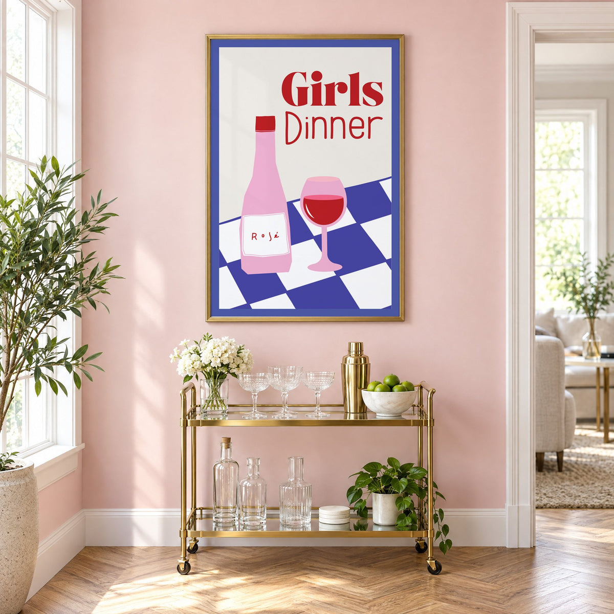 Girls Dinner rosé bottle on checkered table print in a brass frame on a blush pink wall above a gold bar cart with glassware