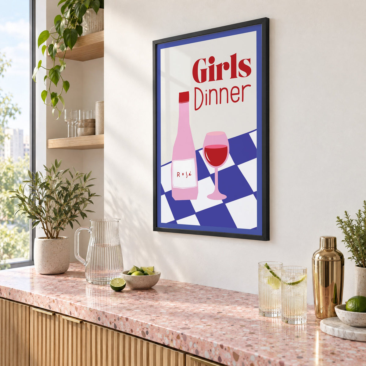 Girls Dinner rosé bottle on checkered table print in a black frame above a pink terrazzo cocktail counter with limes, seen at an angle