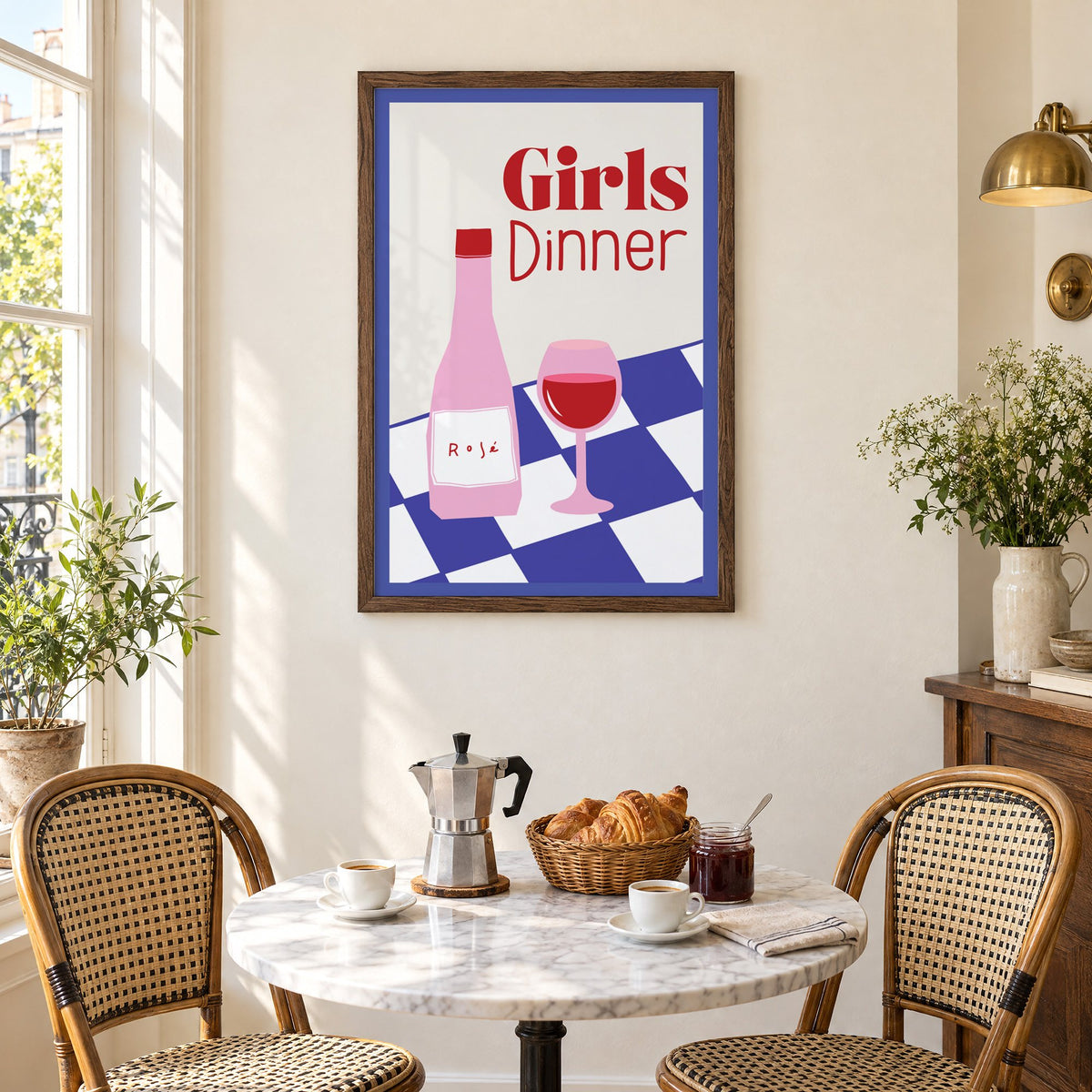 Girls Dinner rosé bottle on checkered table print in a walnut frame above a marble bistro table with croissants and rattan chairs