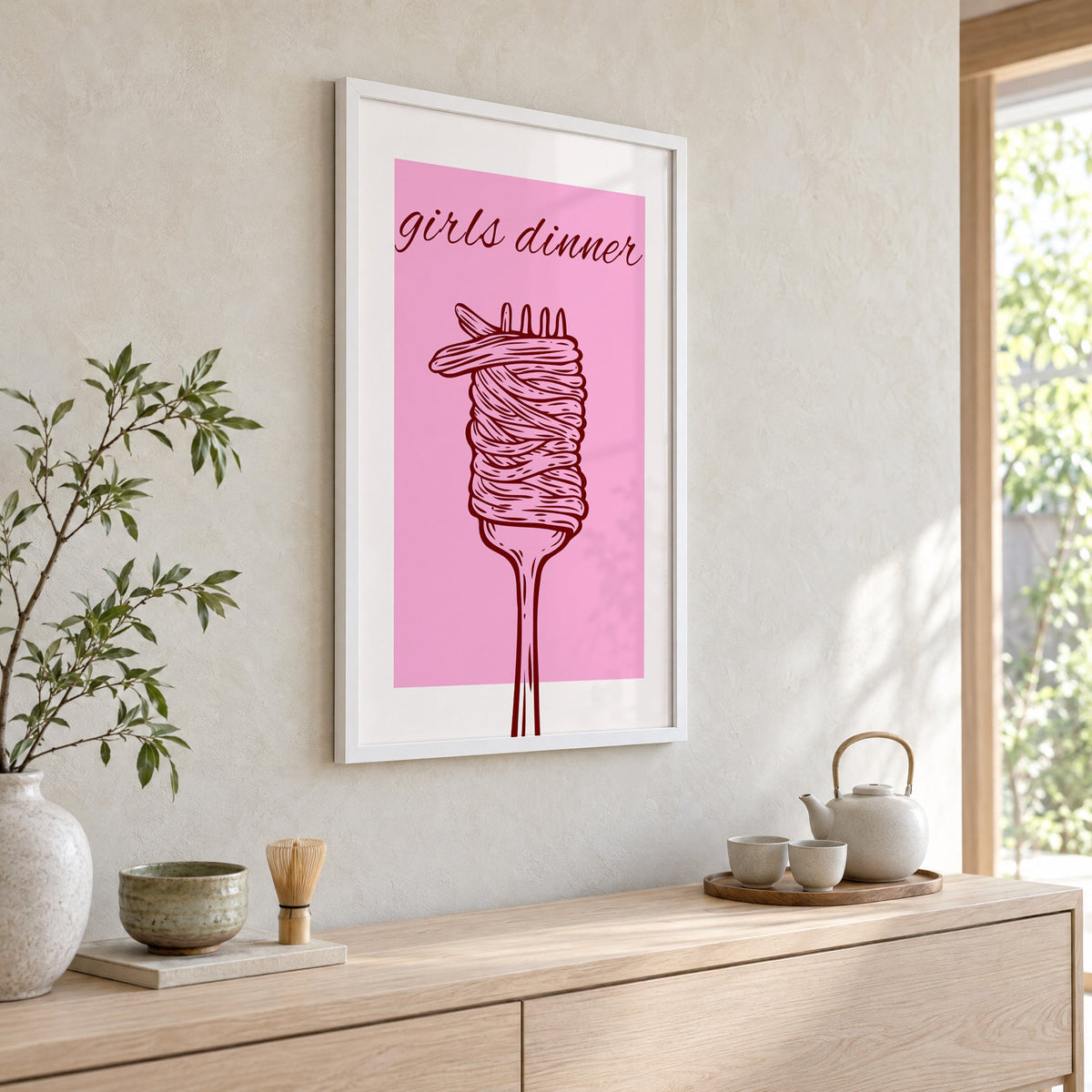 Girls dinner spaghetti fork pink print in a white frame above a pale wood console with a matcha tea set