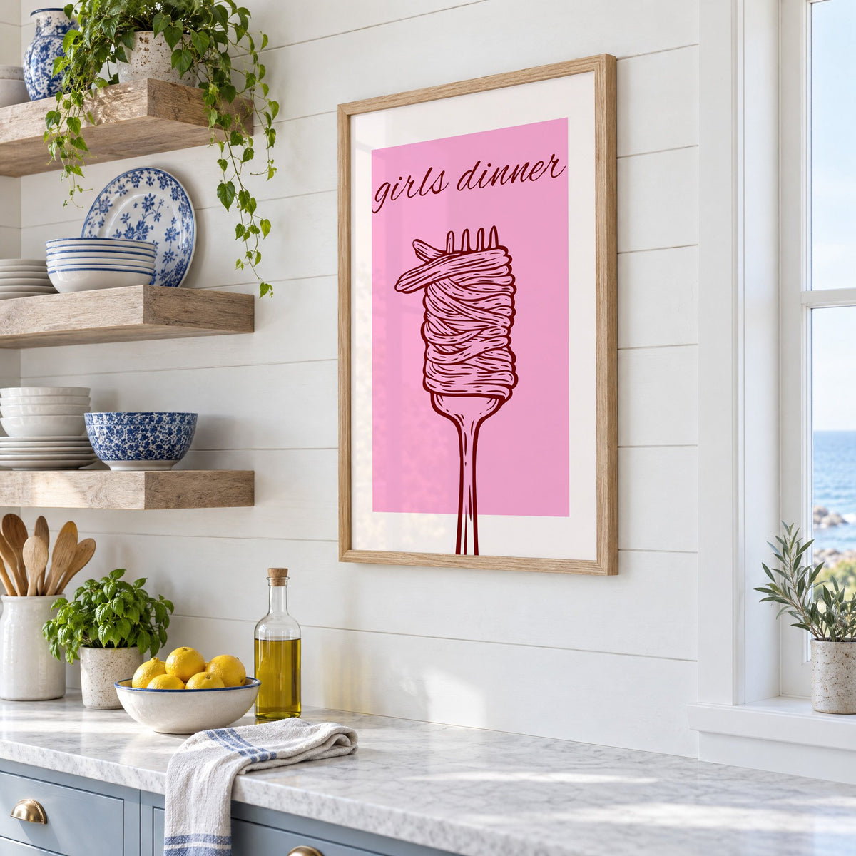 Girls dinner spaghetti fork pink print in an oak frame in a white coastal kitchen beside blue and white plates