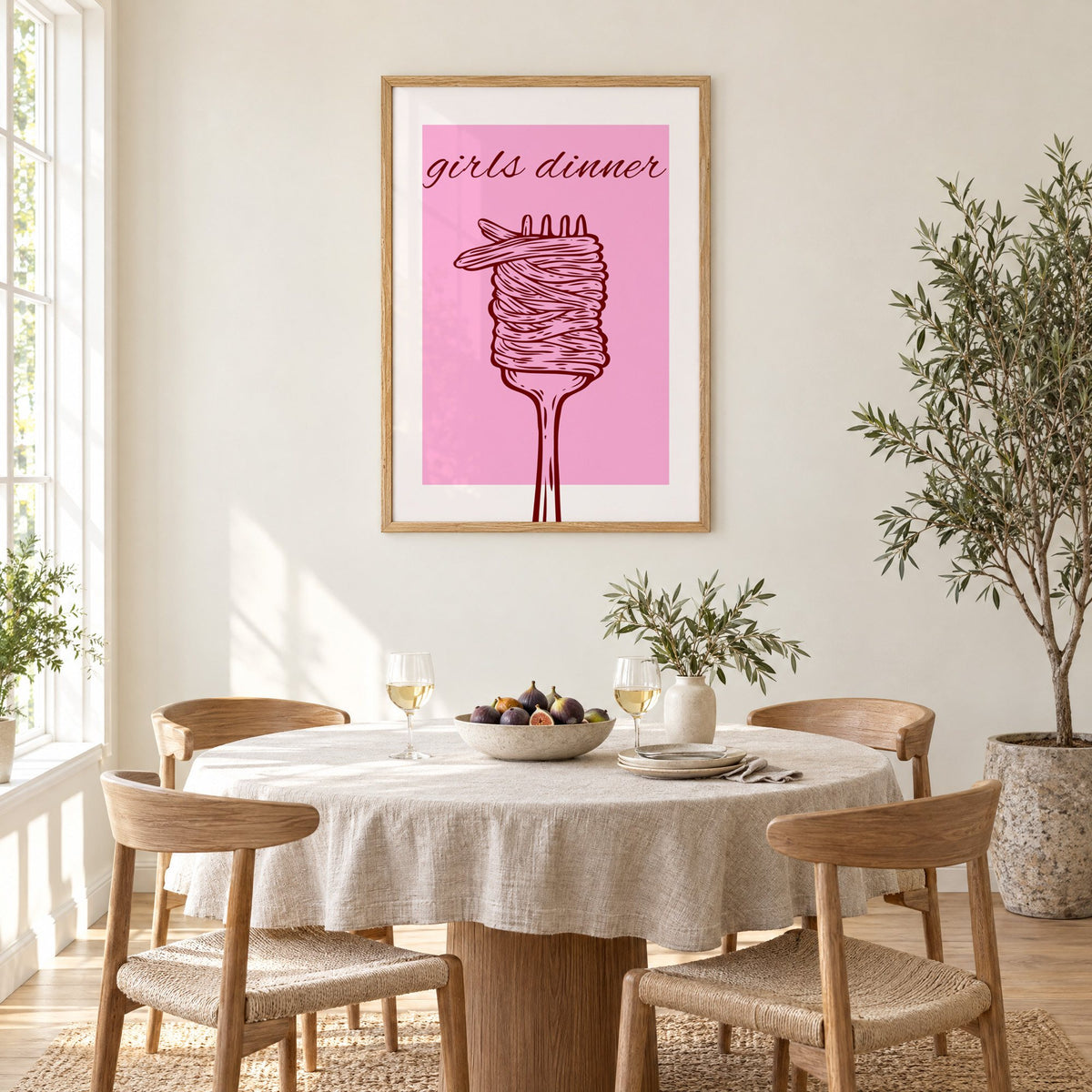 Girls dinner spaghetti fork pink print in an oak frame above a round linen-covered dining table with figs and wine