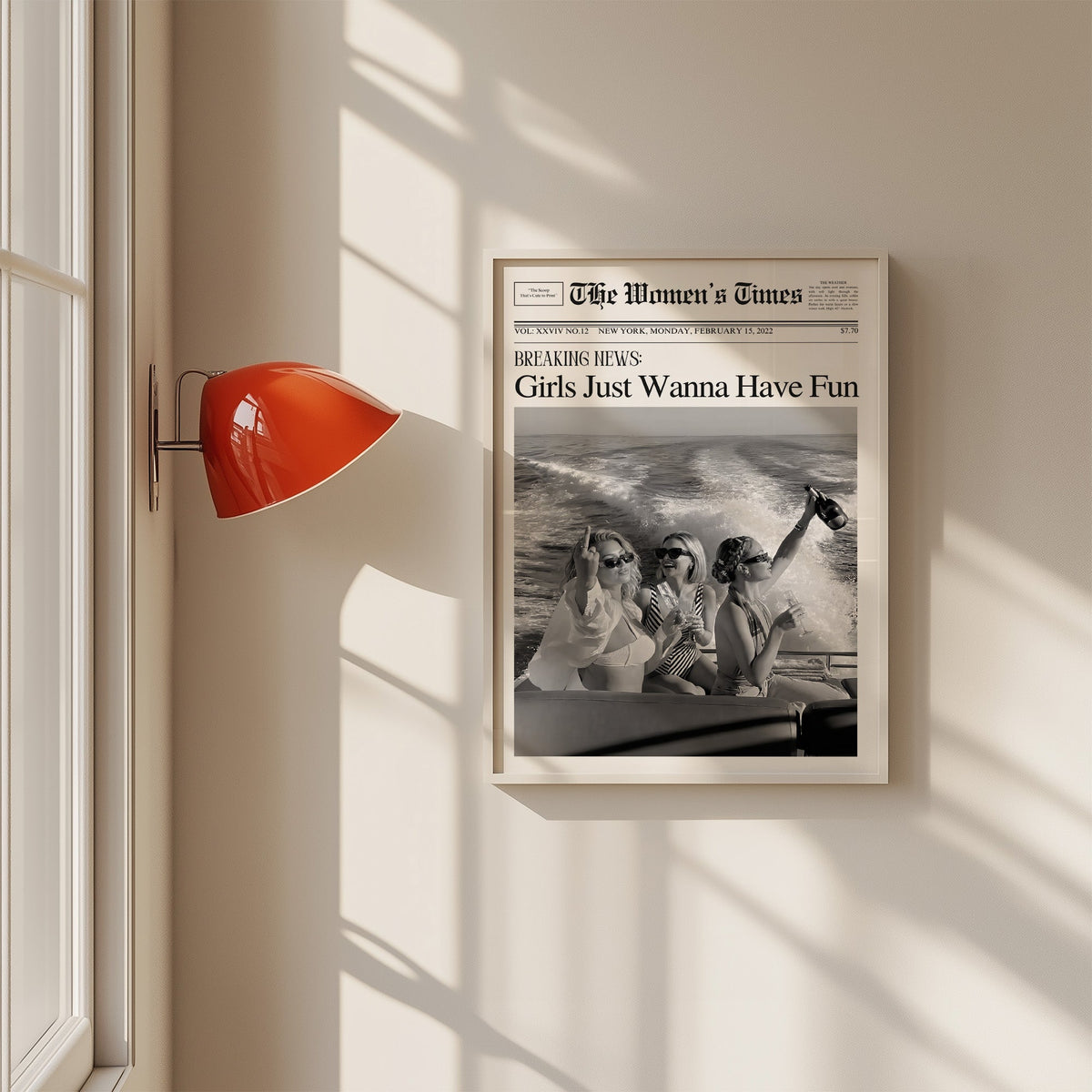 Mock front page with three women on a yacht print in a white frame on a sunlit wall beside a red sconce