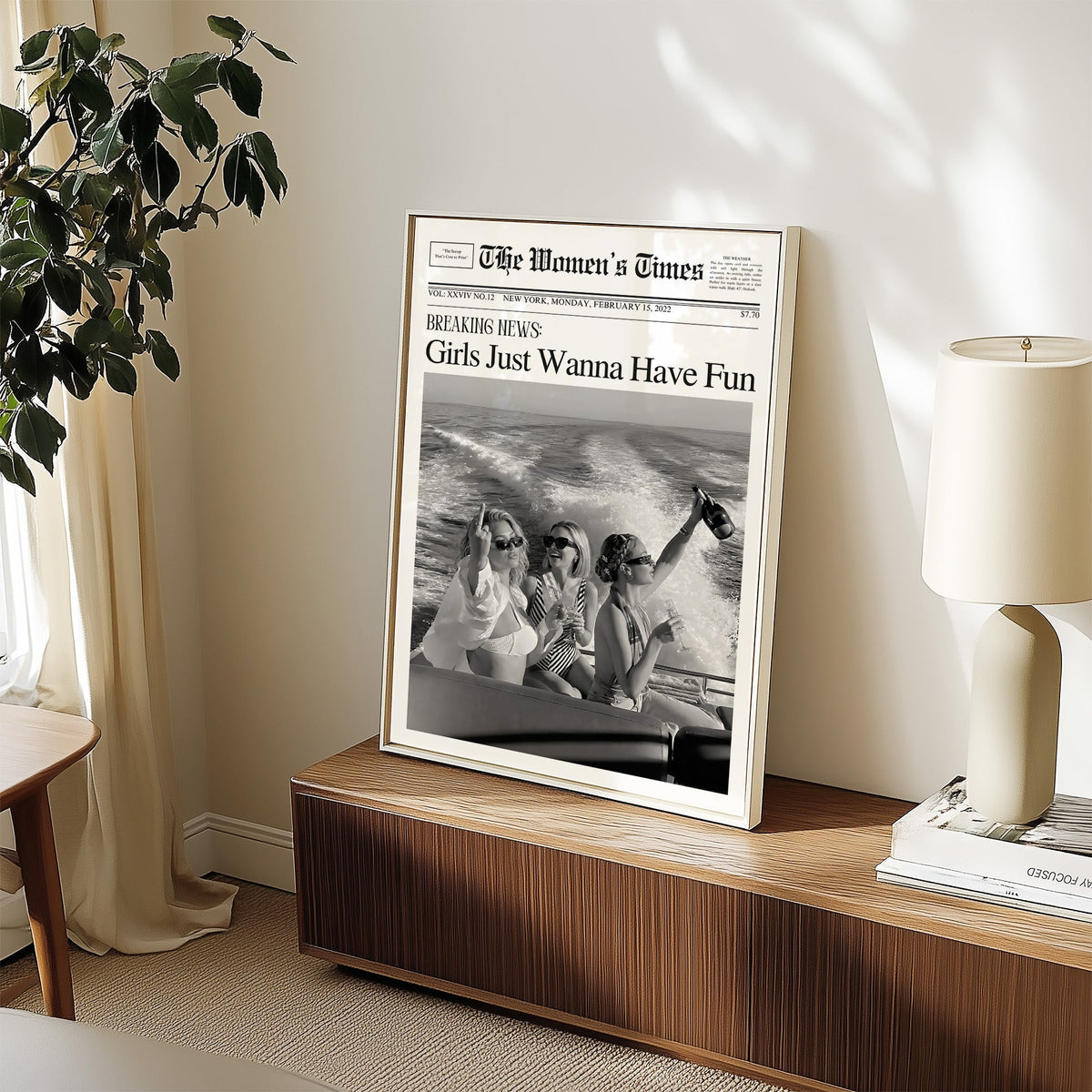 Mock front page with three women on a yacht print in a white frame on a walnut sideboard beside a ceramic lamp