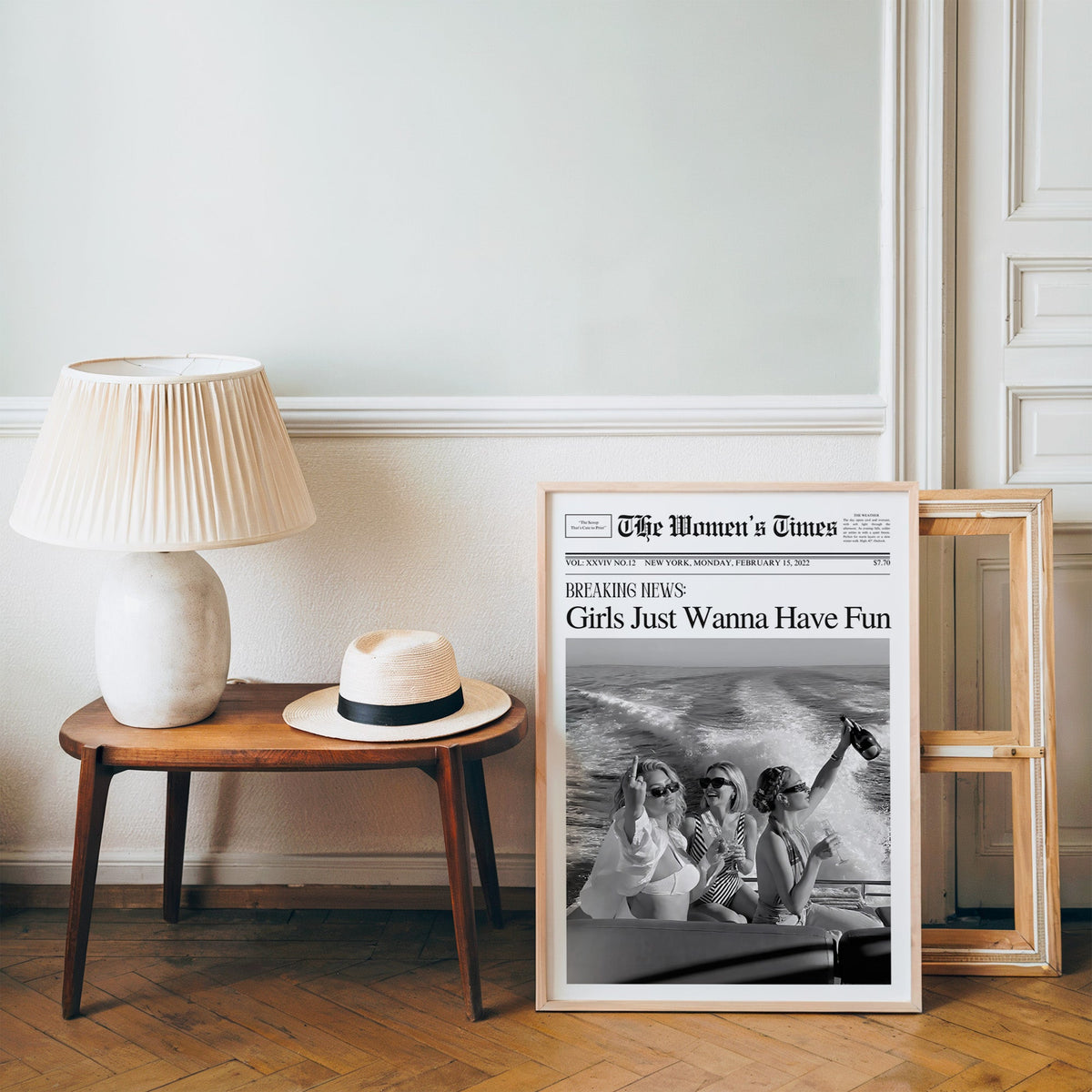 Mock front page with three women on a yacht print in a pine frame on a wood floor beside a lamp and straw hat