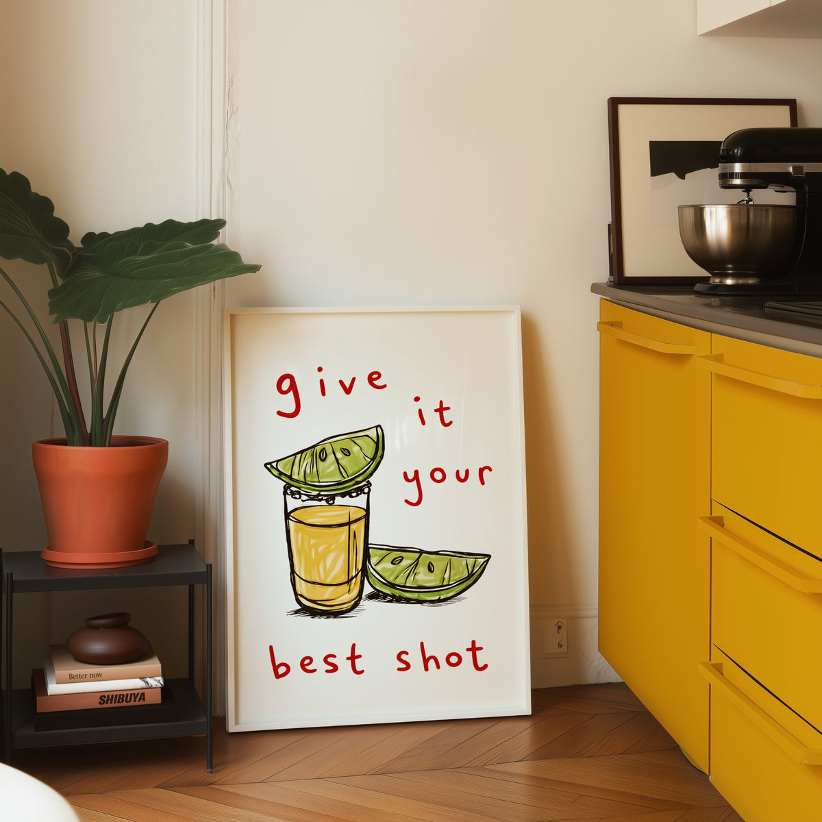 Tequila shot print in a white frame leaning on parquet beside a bright yellow kitchen