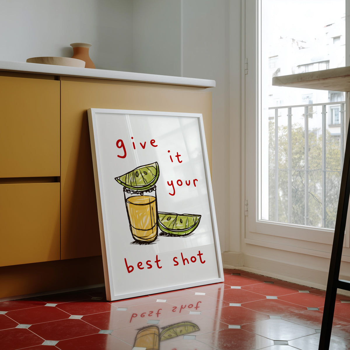 Tequila shot print in a white frame against yellow cabinets on a red tiled floor