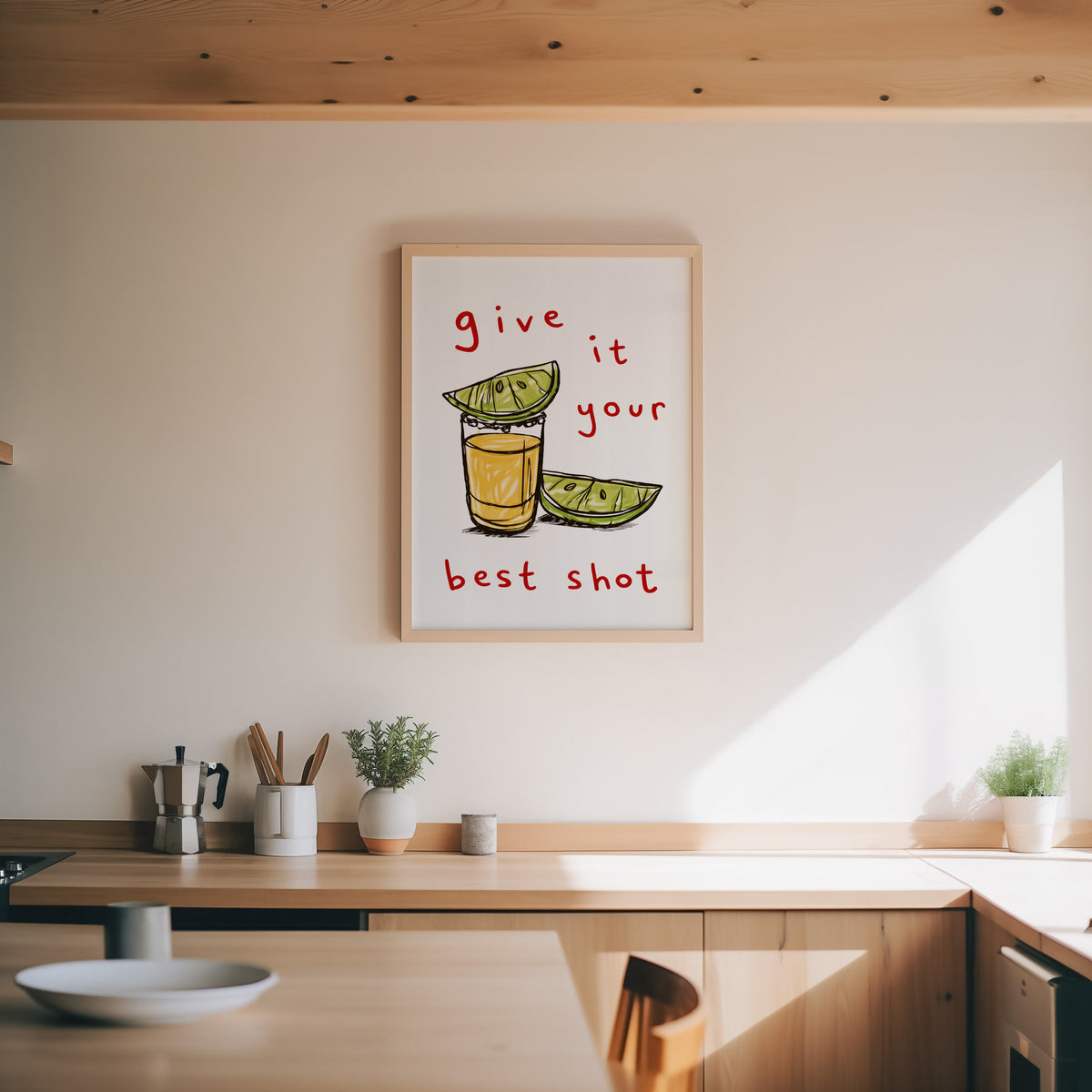 Tequila shot print in an oak frame above a wood counter with a moka pot and herbs
