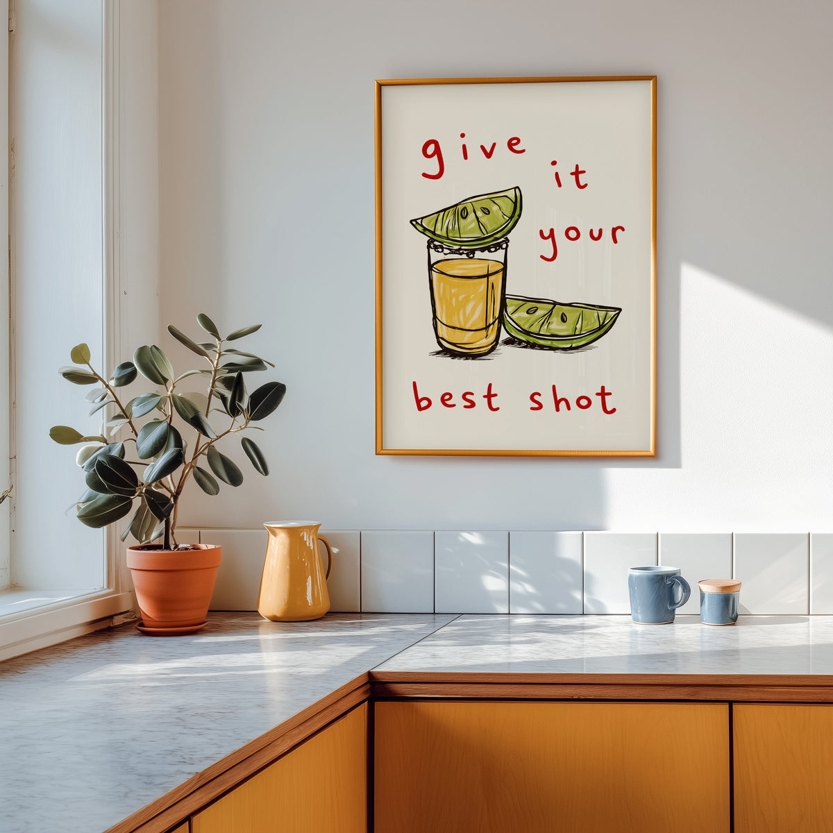 Tequila shot print shown in a gold frame above a marble counter with a yellow ceramic jug