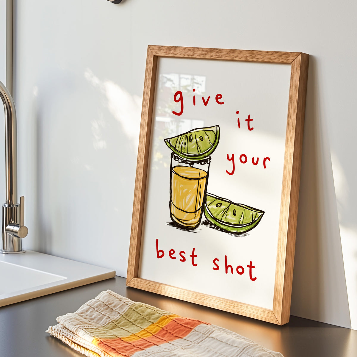 Tequila shot print in an oak frame by the kitchen sink beside a striped tea towel