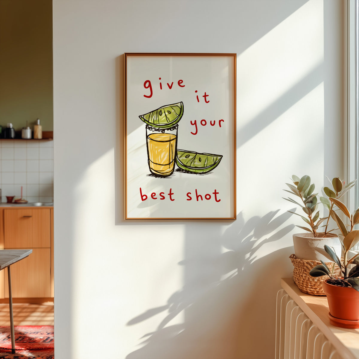 Tequila shot print shown in a gold frame in sunlight with plants and a kitchen beyond