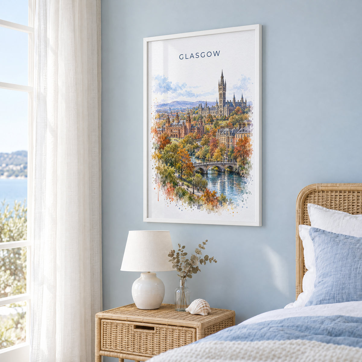 Glasgow watercolor print in a white frame on a pale blue wall beside a rattan bed in a coastal bedroom