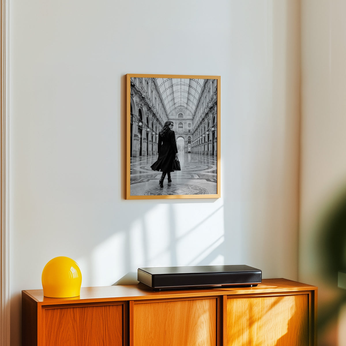 Black and white woman in a glass arcade print in an oak frame above a teak sideboard with a yellow glass lamp