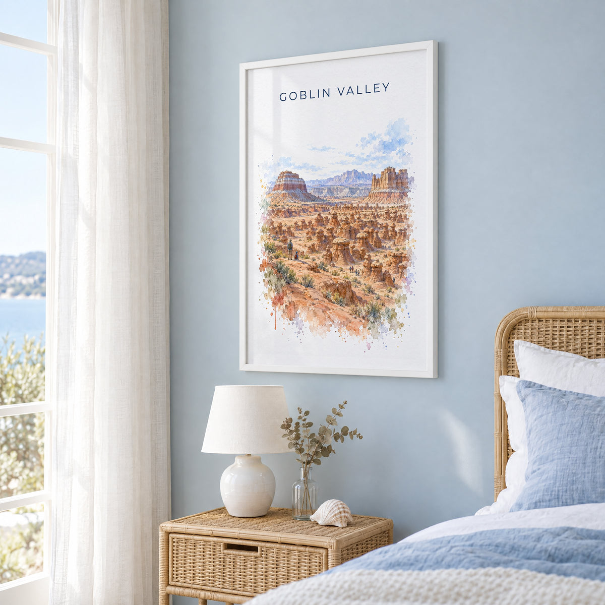 Goblin Valley State Park watercolor print in a white frame on a pale blue wall beside a rattan bed in a coastal bedroom