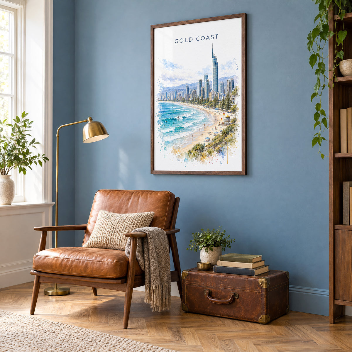 Gold Coast watercolor print in a walnut frame on a blue wall above a leather armchair in a reading nook