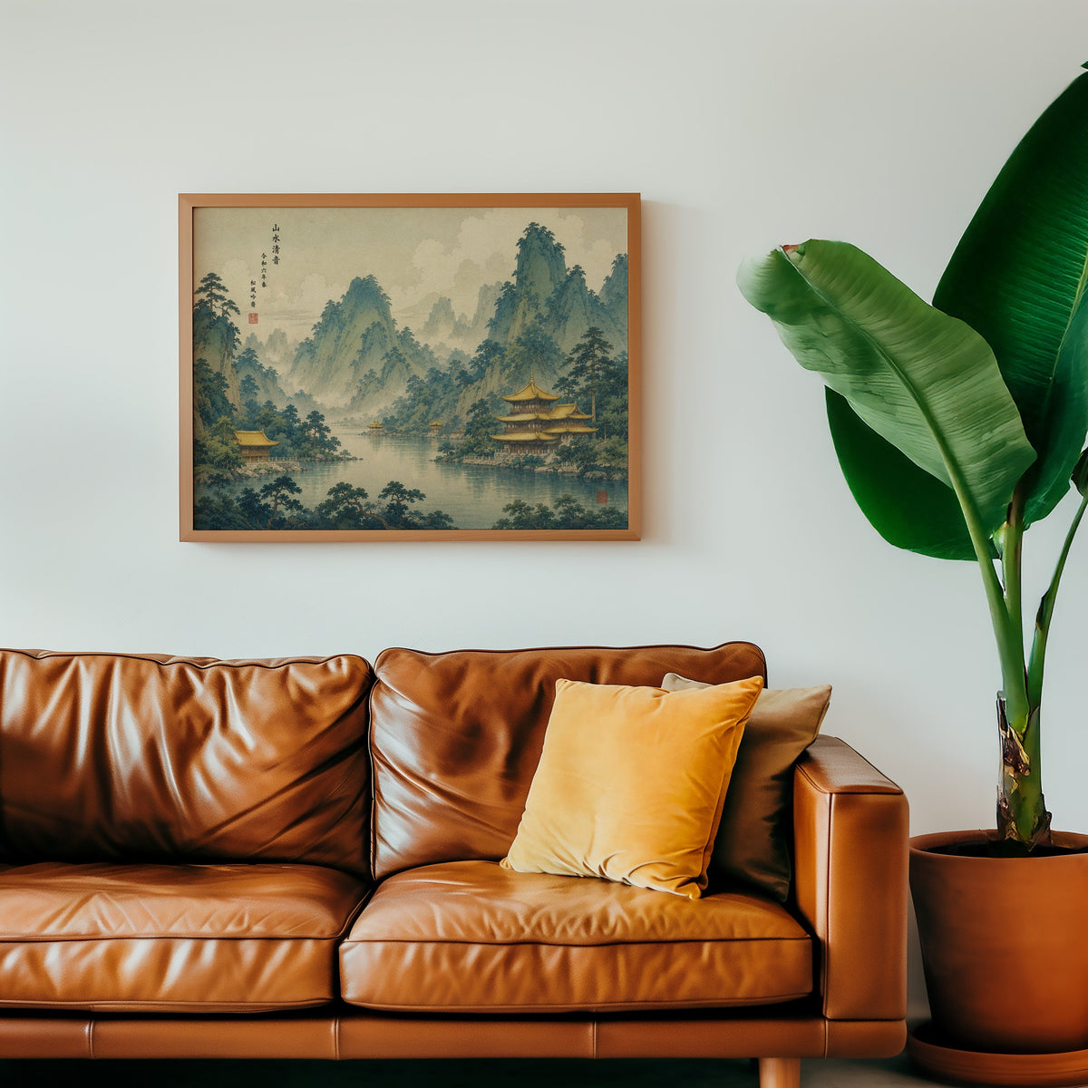 Golden temples below green mountains print in a warm oak frame above a cognac leather sofa with a mustard pillow