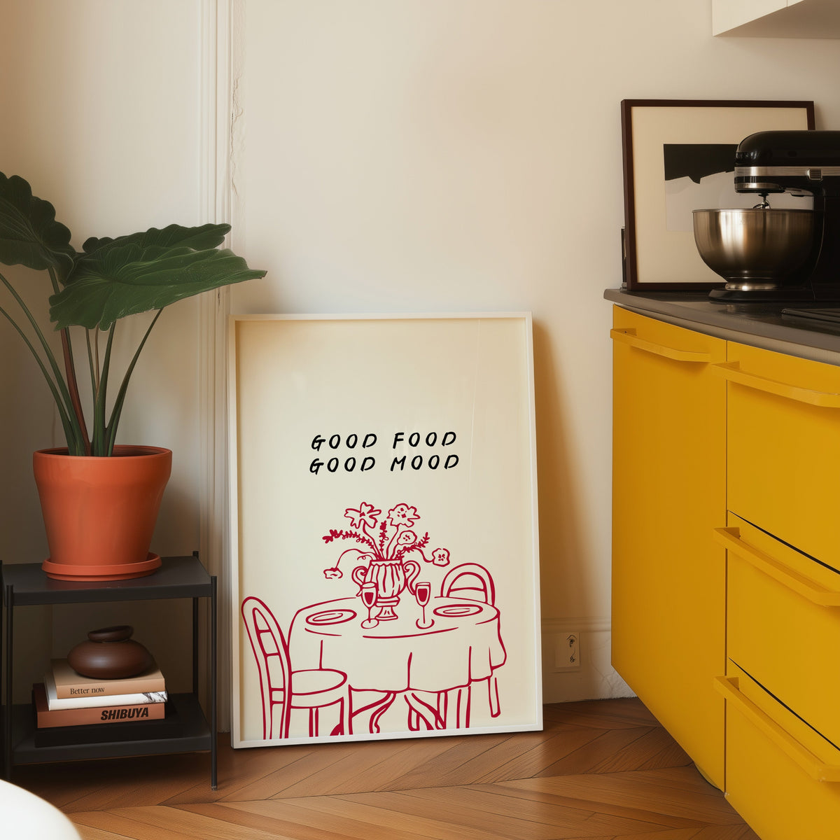 Good Food Good Mood print in a white frame leaning on parquet by a yellow kitchen