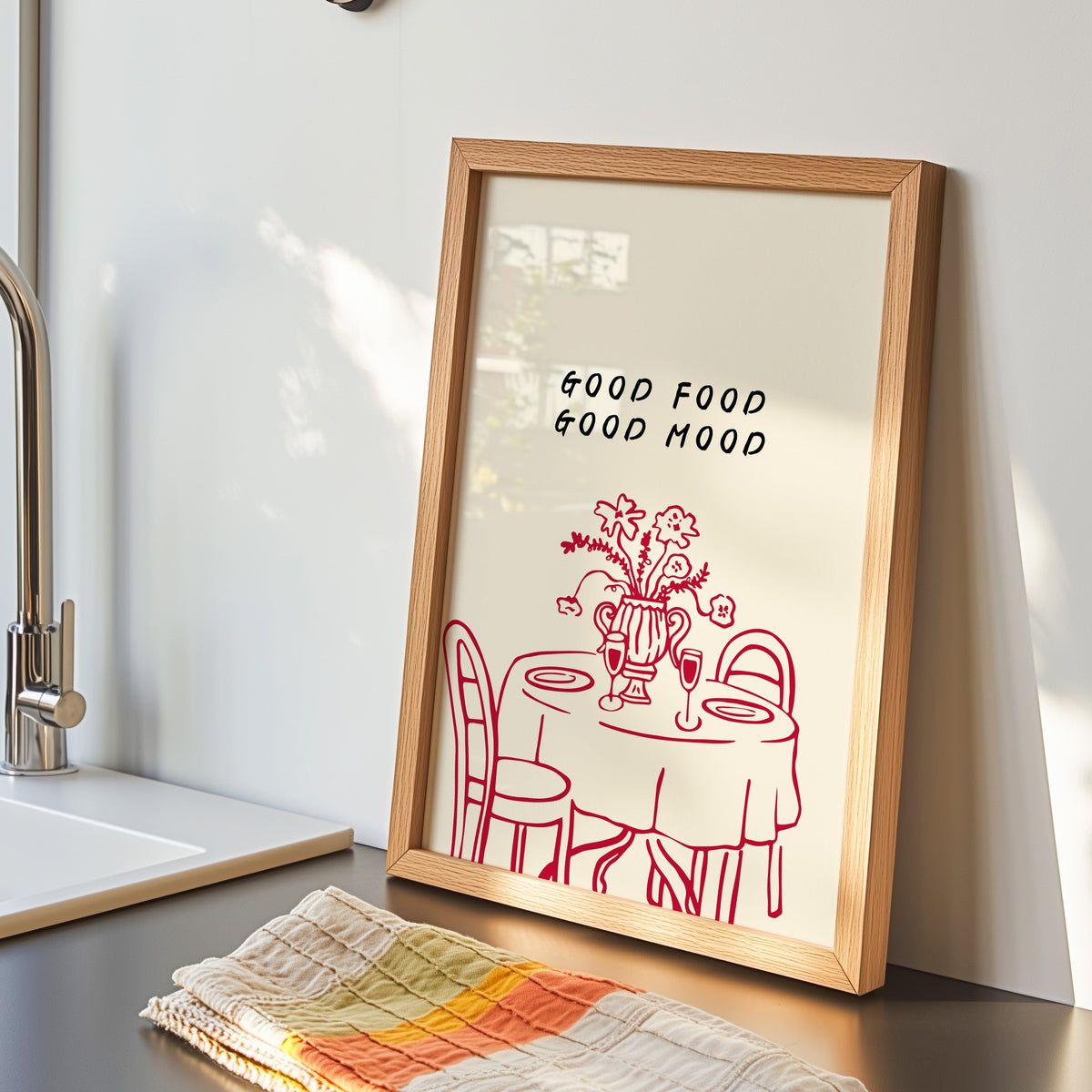 Good Food Good Mood print in an oak frame by the kitchen sink with a striped tea towel