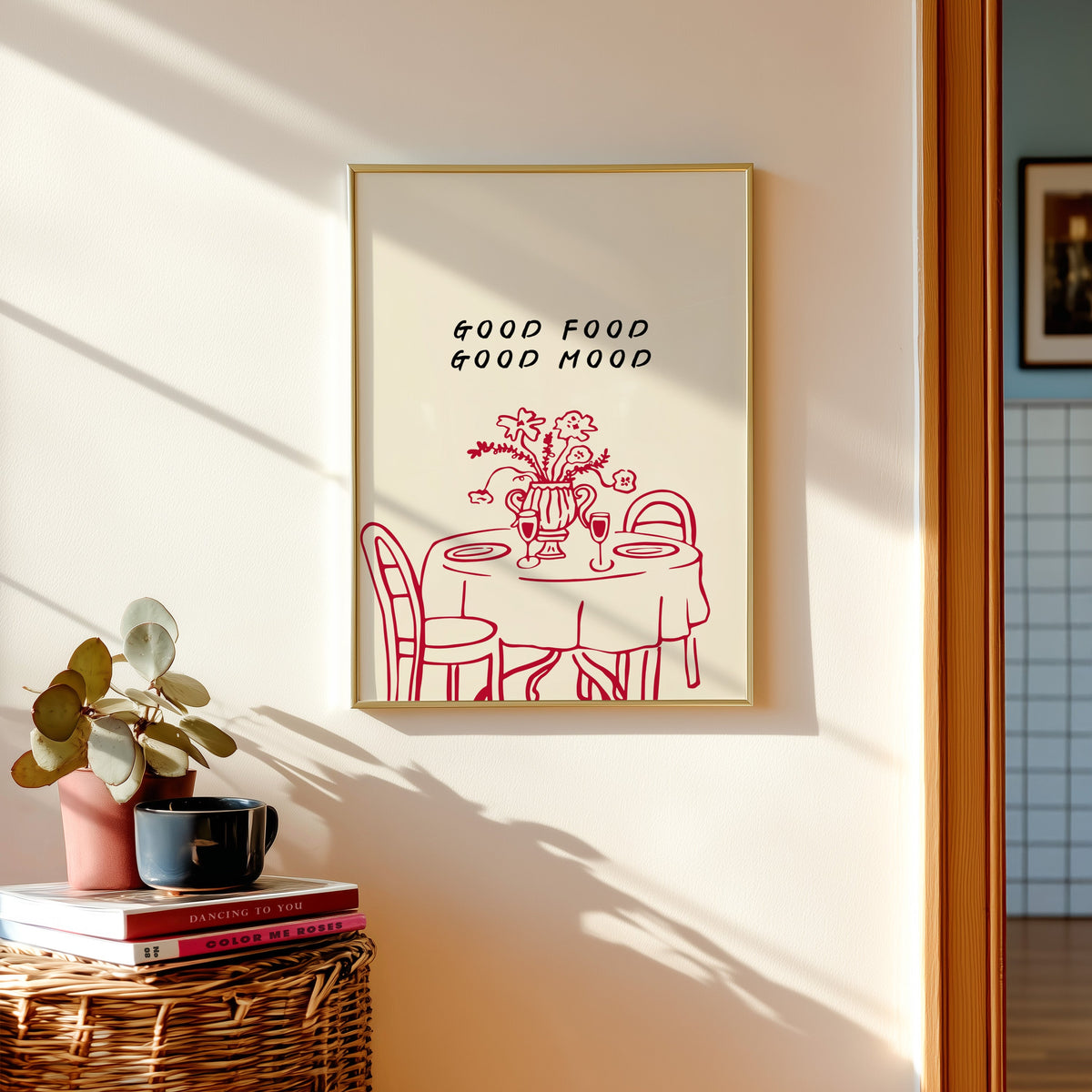 Good Food Good Mood print in a gold frame above a basket of books and a pilea plant