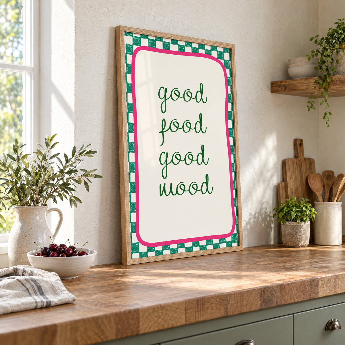 Good food good mood checkered print in an oak frame leaning on a butcher block island beside a bowl of cherries