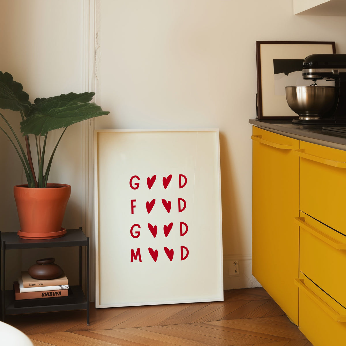Good Food Good Mood print in a white frame leaning on parquet beside a bright yellow kitchen