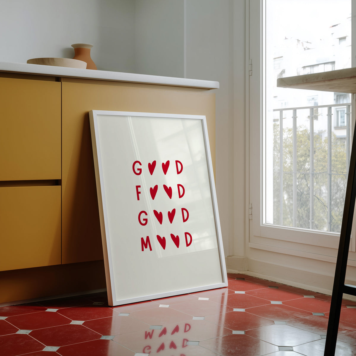 Good Food Good Mood print in a white frame against yellow cabinets on a red tiled floor