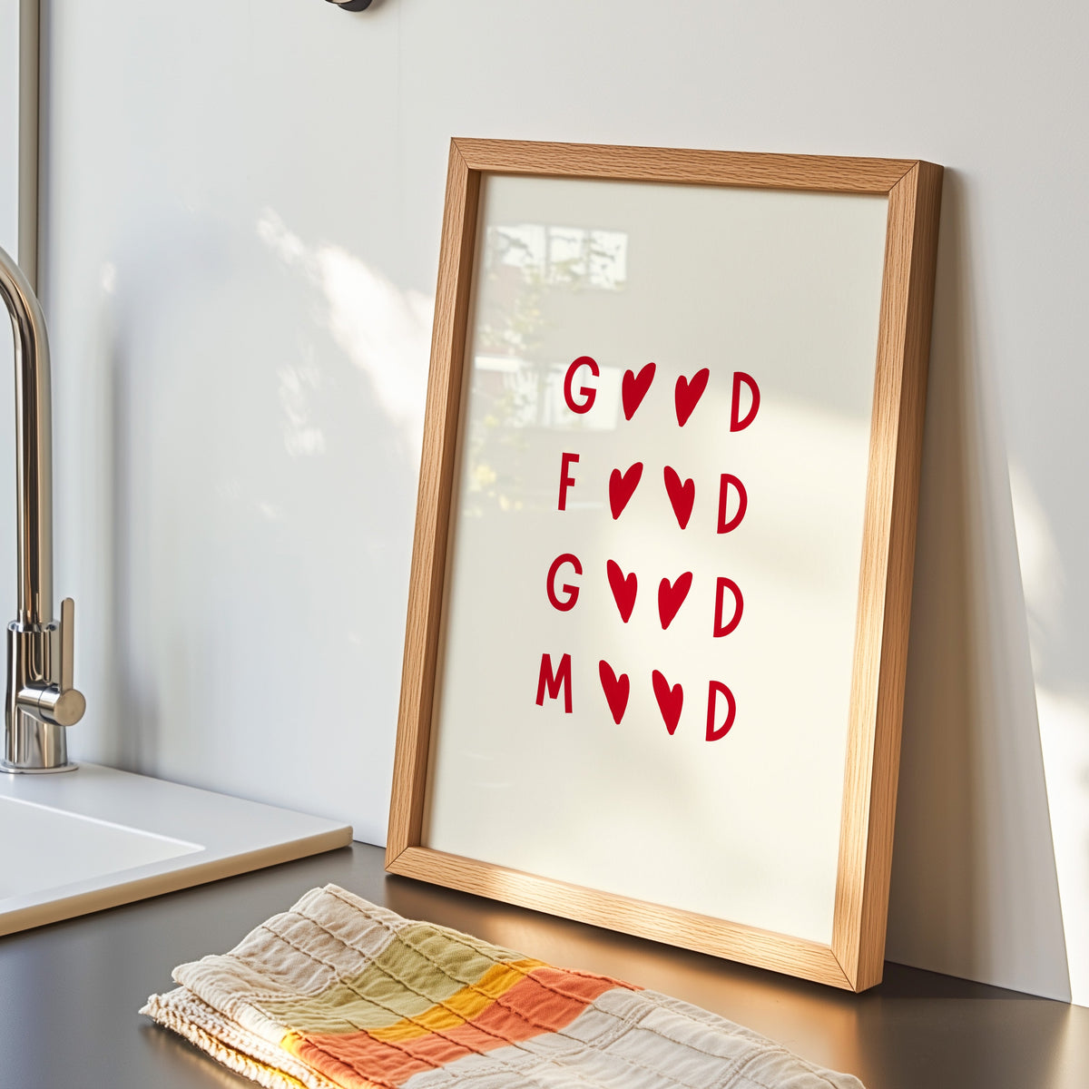 Good Food Good Mood print in an oak frame by the kitchen sink beside a striped tea towel
