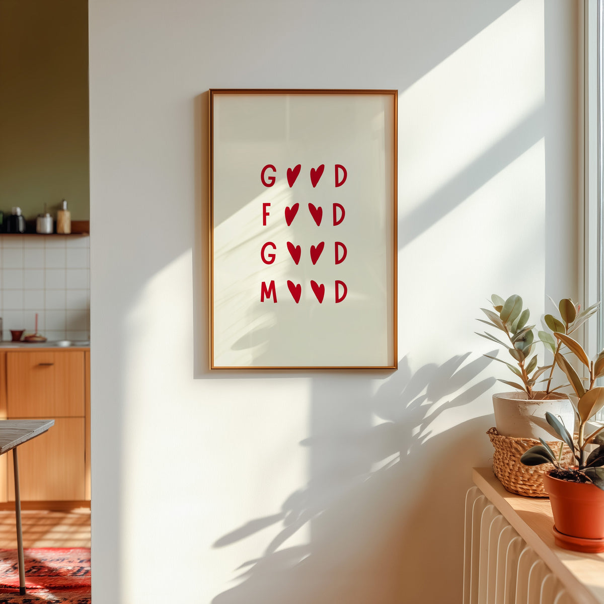Good Food Good Mood print shown in a gold frame in sunlight with plants and a kitchen beyond