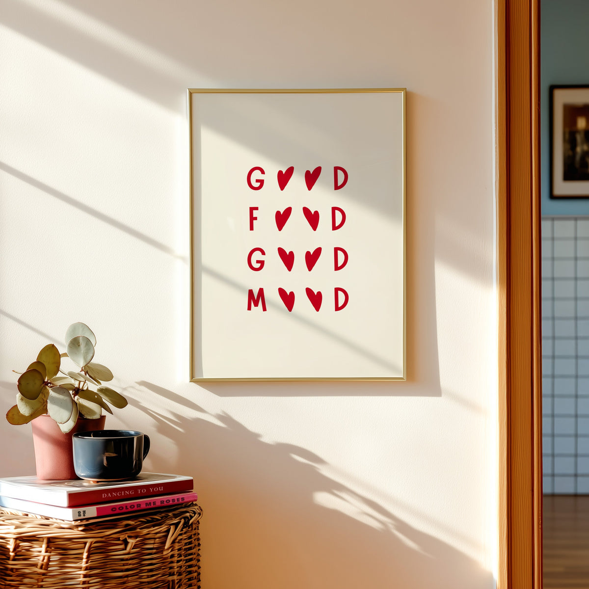 Good Food Good Mood print shown in a gold frame above a basket of books and a pilea plant