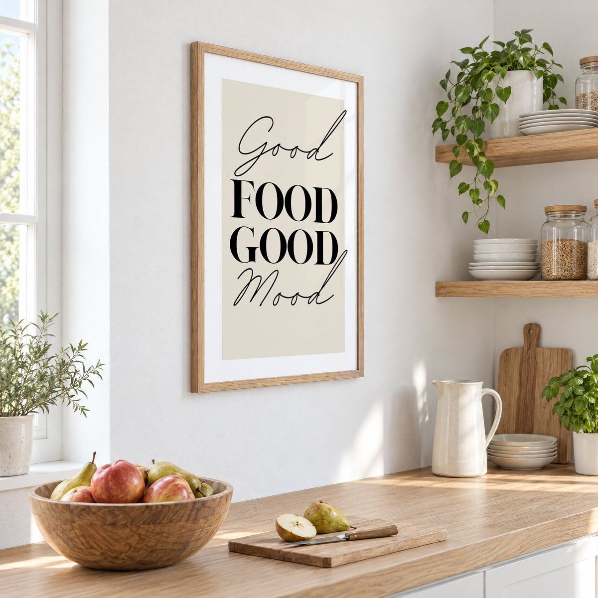 Good FOOD GOOD Mood serif script print in an oak frame on a white kitchen wall above a counter with apples and pears, seen at an angle