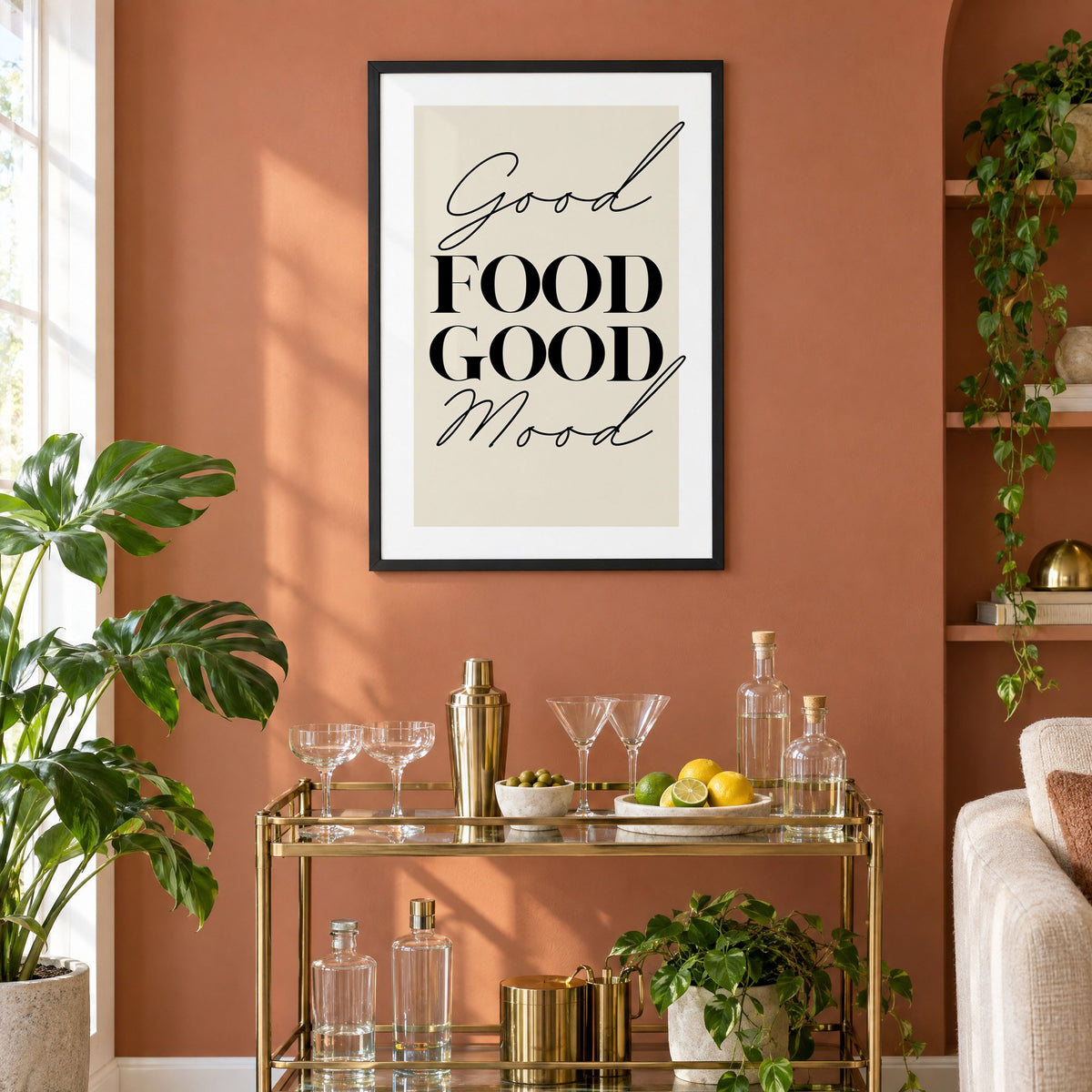 Good FOOD GOOD Mood serif script print in a black frame on a terracotta wall above a brass bar cart with coupes and citrus
