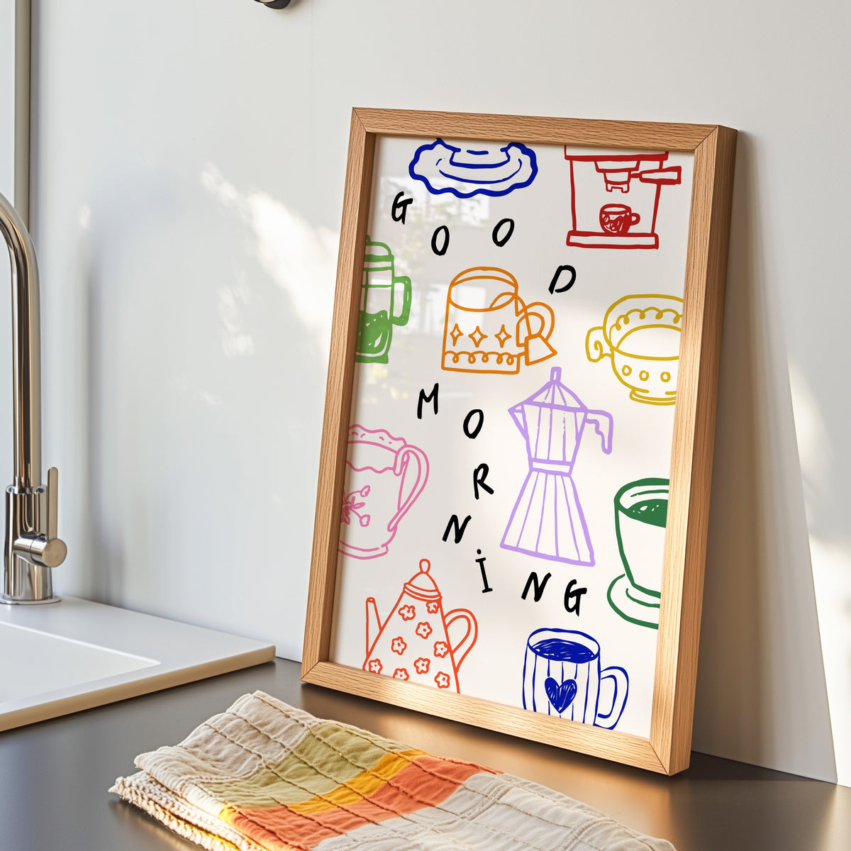 Good Morning coffee print in an oak frame by the kitchen sink beside a striped tea towel