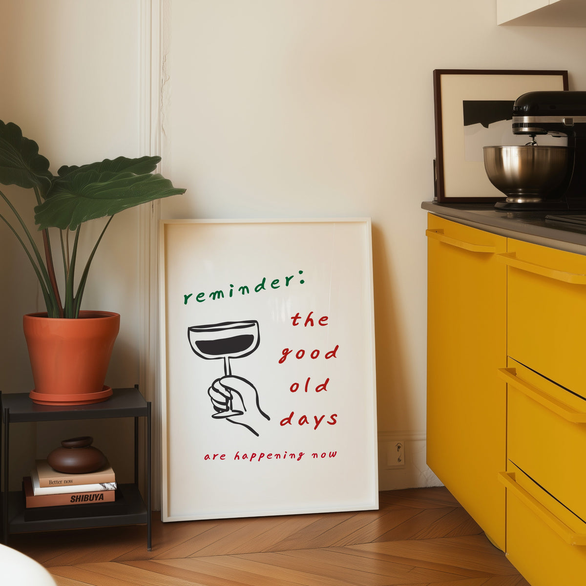 Good Old Days print in a white frame leaning on parquet beside a bright yellow kitchen